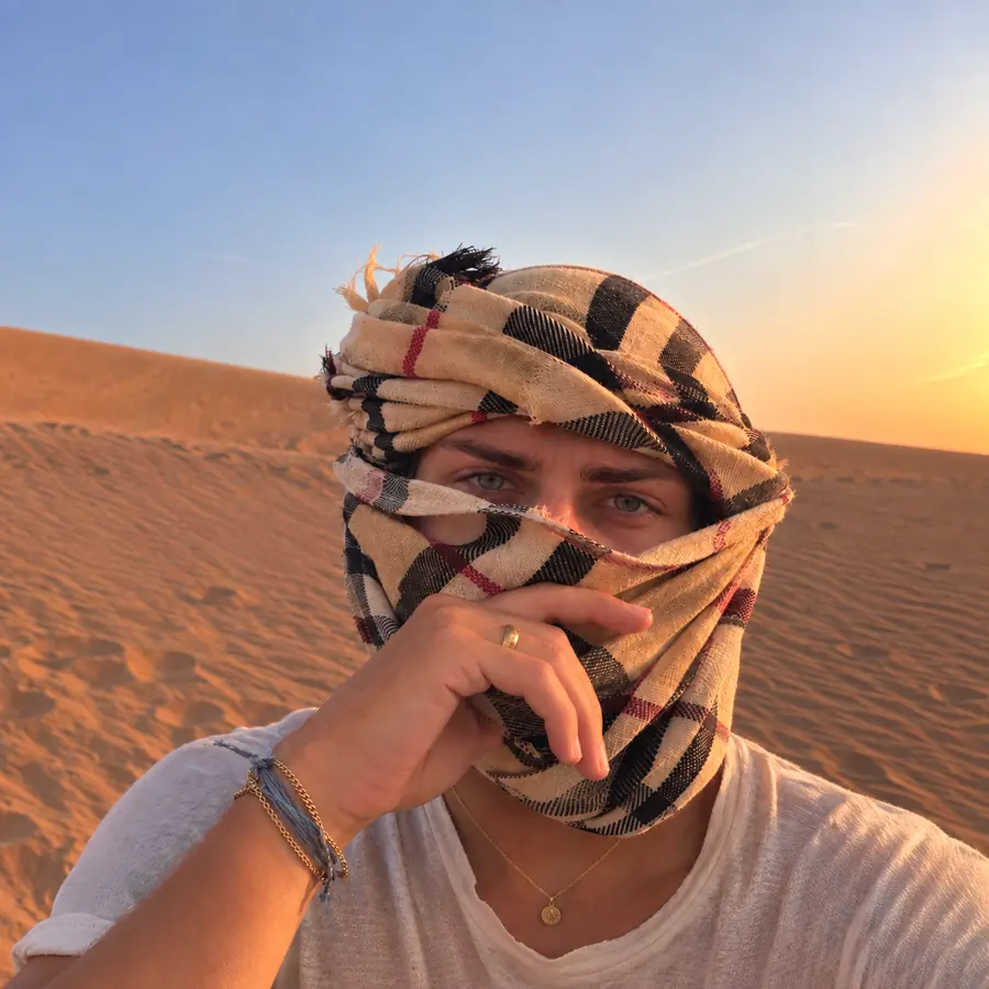 Brennan Harmatz in the desert at sunset with a scarf over his face