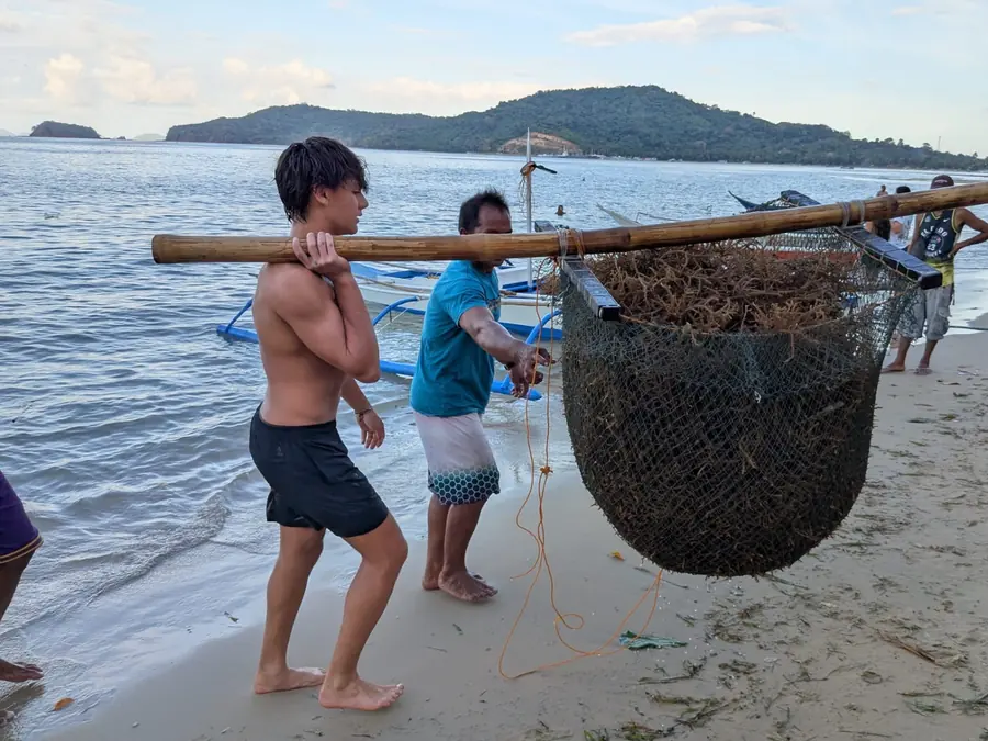 Brennan Harmatz carrying a fishing net on the beach with a local fisherman