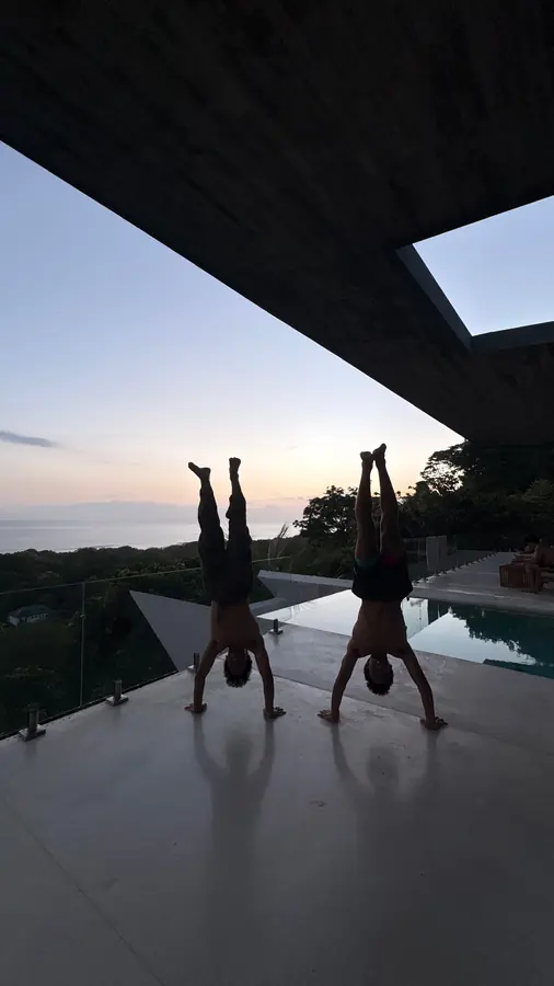 Brennan Harmatz and a friend doing handstands by an infinity pool at dusk