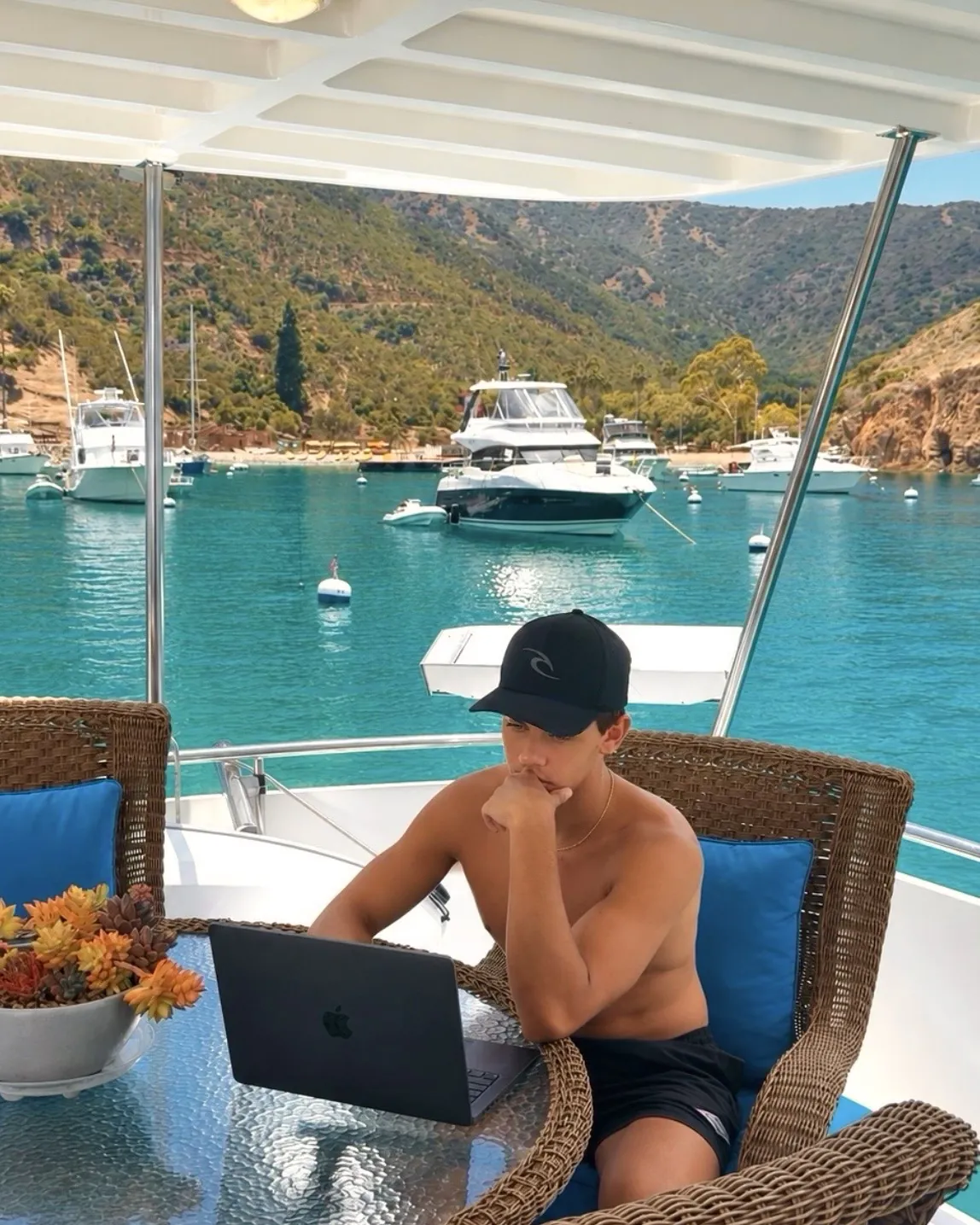 Brennan Harmatz working on a laptop on a boat in a cove