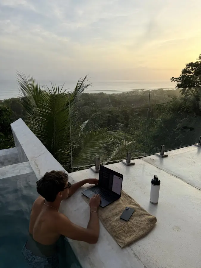 Brennan Harmatz working on a laptop on a terrace at sunset above the jungle